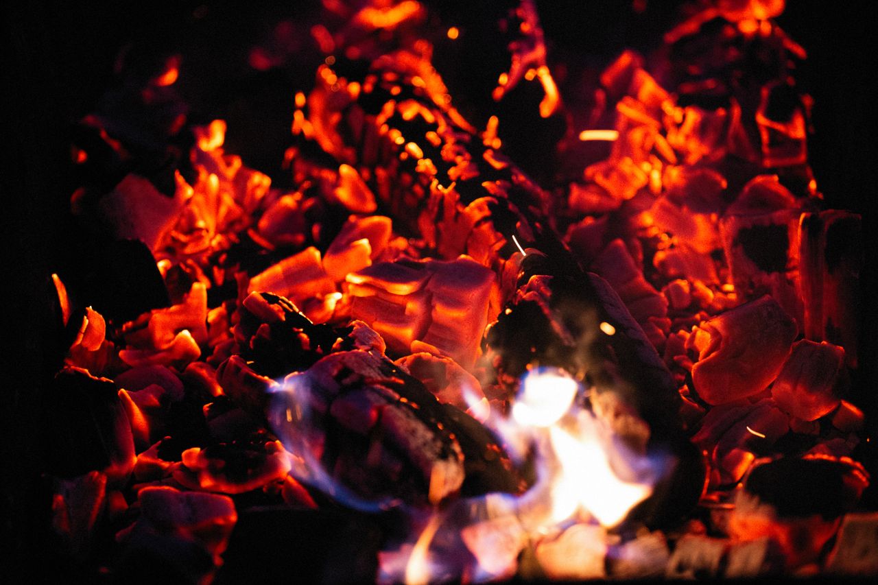 About An intense close-up of glowing hot coals and vibrant flames at night, creating a fiery spectacle.